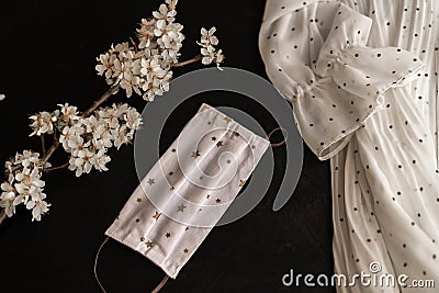 Medical mask with asterisks on a black background, a branch of a blossoming tree and a polka dot dress. Stock Photo