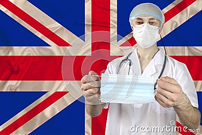 Medical mask in the hands of a doctor against the background of the national flag of Great Britain, concept of protection against Stock Photo