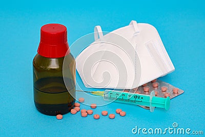 Medical pills are scattered on a blue background. Glass vial, syringe and face shield Stock Photo