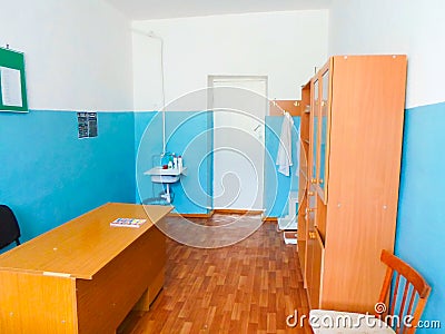 Medical room at school with a cupboard table and wash basin. blue and white walls, medical gowns on the hanger Editorial Stock Photo