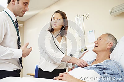 Medical Staff On Rounds Examining Senior Male Patient Stock Photo