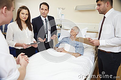 Medical Staff On Rounds Standing By Male Patient's Bed Stock Photo