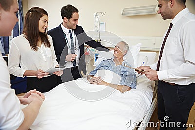 Medical Staff On Rounds Standing By Male Patient's Bed Stock Photo