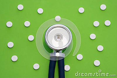 The medical stethoscope is on a green background surrounded by white round pills. The concept of a minimalistic photo to indicate Stock Photo