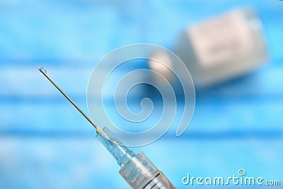 Medical vial of injectable medicine and hypodermic needle on a blue mask Stock Photo