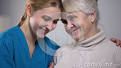 Medical worker hugging and supporting smiling elderly lady in nursing home Stock Photo