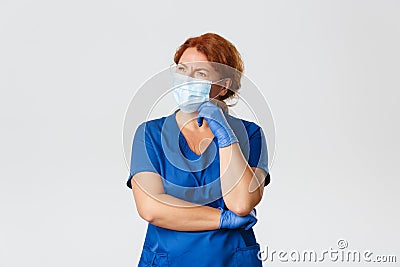 Medical workers, coronavirus concept. Confused and thoughtful female redhead doctor, nurse in scrubs, face mask and Stock Photo