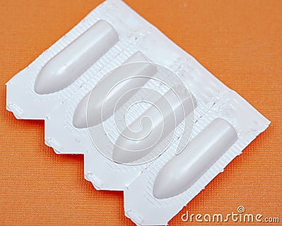 Medication in disposable plastic suppository moulds on orange. Rectal drug administration Stock Photo