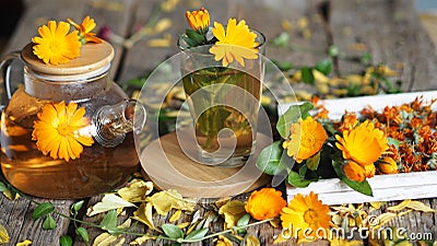 Medicinal autumn background. Herbal healthy marigold tea with a teapot, dried and fresh flowers on an autumn wooden background Stock Photo