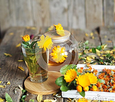 Medicinal autumn background. Herbal healthy marigold tea with a teapot, dried and fresh flowers on an autumn wooden background Stock Photo