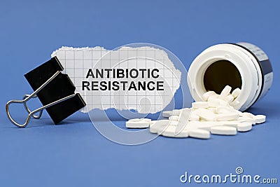 On the blue surface lies a jar of pills and a clip with paper on which is written - ANTIBIOTIC RESISTANCE Stock Photo