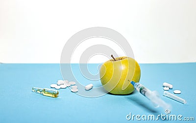 Medicine concept with fresh injured apple, tablets, ampoule and syringe. Genetically modified fruit on light blue background Stock Photo