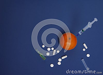 Medicine concept with injected mandarin, tablets, ampoule and syringe. Genetically modified fruit on classic blue background Stock Photo