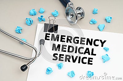 On the table is a stethoscope, blue crumpled pieces of paper and a sign with the inscription - EMERGENCY MEDICAL SERVICE Stock Photo