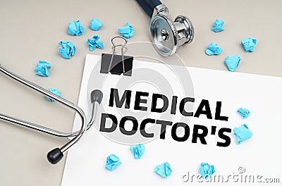 On the table is a stethoscope, a pen, blue crumpled pieces of paper and a sign with the inscription - MEDICAL DOCTORS Stock Photo