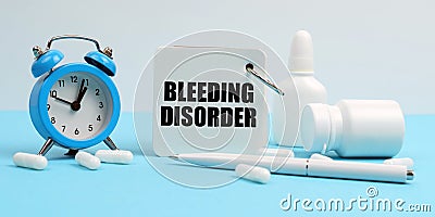 On a blue surface lie pills, an alarm clock and a notebook with the inscription - Bleeding Disorder Stock Photo