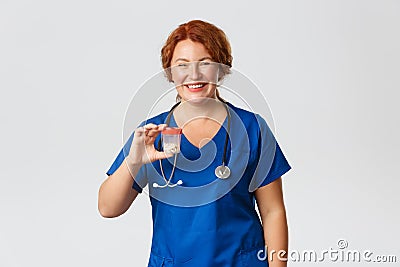 Medicine, healthcare and coronavirus concept. Cheerful smiling female meical worker, doctor in scrubs showing container Stock Photo
