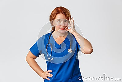 Medicine, healthcare and coronavirus concept. Excited middle-aged female medical worker zipping her lips as gossiping Stock Photo