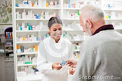 Smiling young female pharmacist giving prescription medication pills to senior male patient Stock Photo