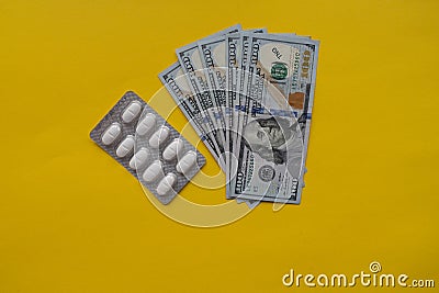 Medicine pills and 100 dollar banknote on yellow background. Healthcare insurance and medical treatment cost concept Stock Photo