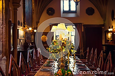 Medieval british castle interior dining table with plates, flowers and lamps. Warm light. Selective focus. copy space Editorial Stock Photo