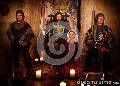 Medieval king with his queen and knights on guard in ancient castle interior Stock Photo
