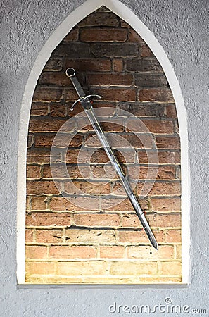 Medieval steel sword against the brick wall background. Ancient shining sword used as decoration Stock Photo