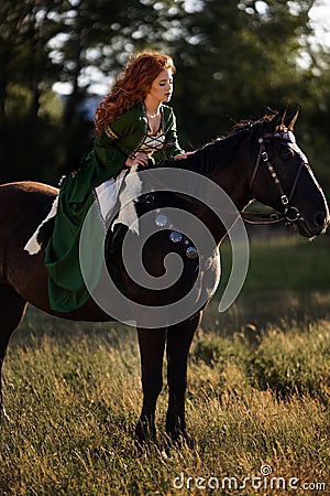 Medieval woman princess in green dress sits astride black steed horse. Stock Photo