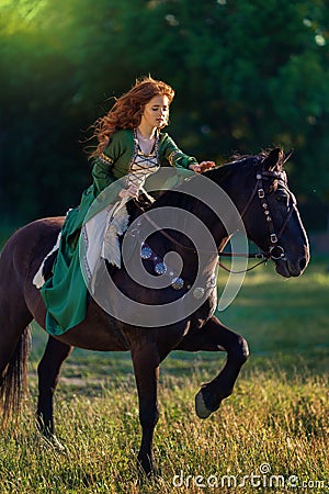 Medieval woman princess in green dress sits astride black steed horse. Stock Photo