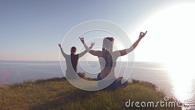 Meditando insieme, giovane e donna al sole che si siedono nella posizione di loto su terra sopra la montagna che esamina mare archivi video Meditando insieme, giovane e donna al sole che si siedono nella posizione di loto su terra sopra la montagna che esamina mare archivi video