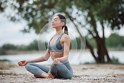Meditating with sounds of nature. Brunette with nice body shape in sportive clothes have fitness day on a beach Stock Photo