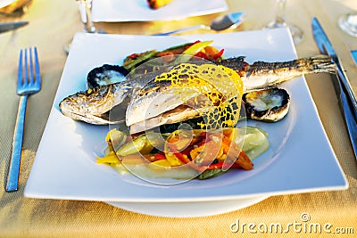 Mediterranean charcoal grilled seabass fish on a white plate with vegetables on the table Stock Photo