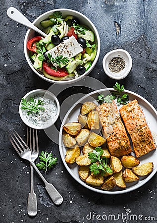 Mediterranean lunch table - baked lemon salmon with potatoes, greek salad, tzadziki sauce on dark background, top view. Flat lay Stock Photo