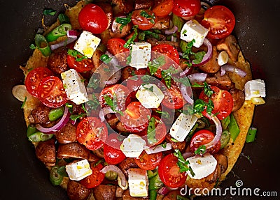 Mediterranean style omelet in frying pan with feta cheese, cherry tomatoes, red onions, mushrooms, spring onions and parsley. Stock Photo