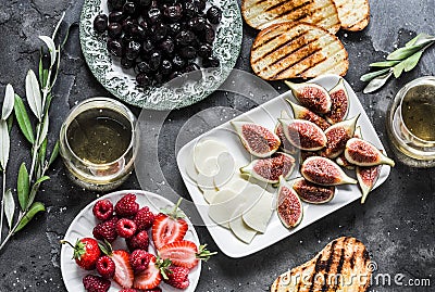Mediterranean style snack appetizers - dried olives, figs, cheese, grilled bread, strawberries, raspberries and white wine on a Stock Photo