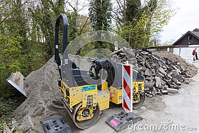 A small asphalt paver stands by the side of the road next to construction debris Editorial Stock Photo