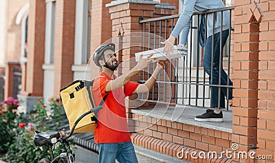 Meeting courier and client. Smiling deliveryman in helmet with big yellow backpack on bicycle delivered pizza to Stock Photo