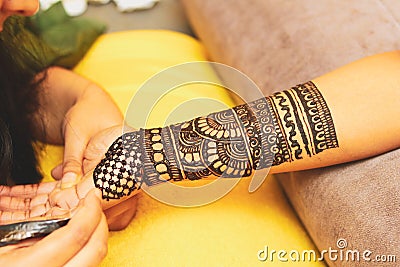 An artist performing mehandi or henna design on female hand. Stock Photo