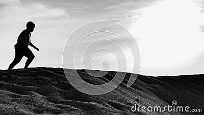 A black and white silhouette view of a young man running freely at the center of desert with sunset as background Editorial Stock Photo