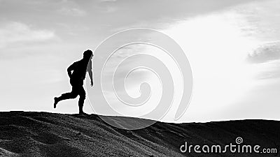 A black and white silhouette view of a young man running freely at the center of desert with sunset as background Editorial Stock Photo