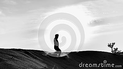 A black and white silhouette view of a young man running freely at the center of desert with sunset as background Editorial Stock Photo