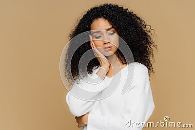 Melancholic sad lonely woman focused down with thoughtful expression, keeps hand on cheek, has calm expression, wears white Stock Photo