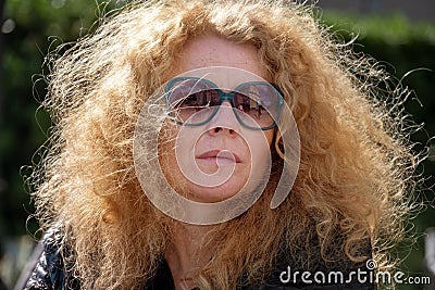 melancholic thoughtful mature woman with sunglasses and red curly hair looks lost in thought into the distance Stock Photo