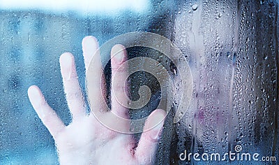 Melancholy and sad young woman at the window in the rain Stock Photo