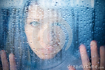 Melancholy and sad young woman at the window in the rain Stock Photo