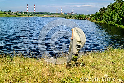 Melee weapons a large knife stuck in the ground on the handle hanging gas mask background plant and pond Stock Photo
