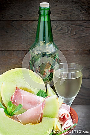 Melon cantaloupe with prosciutto and wine on rustic table Stock Photo