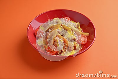 Melting cheddar cheese over the top of french fries covered in spicy sauce with meat and tomatoes. Orange background. Stock Photo