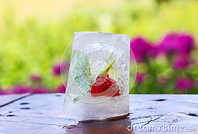 Ice cube with strawberry, lemon and fresh green mint leaves on wooden surface outdoors Stock Photo