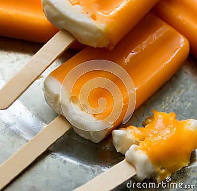 Melting orange creamsicles, one almost eaten, on a galvanized steel plate. Close up view. Stock Photo